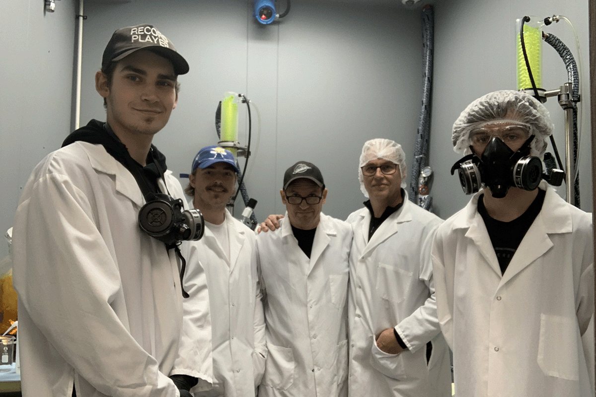 Five members of the Protonify team in white lab coats, hairnets and respirators, standing together in the processing room